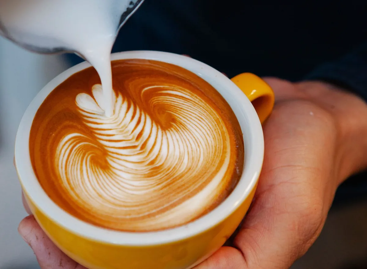 Barista pouring steamed milk into a latte to form a rosetta
