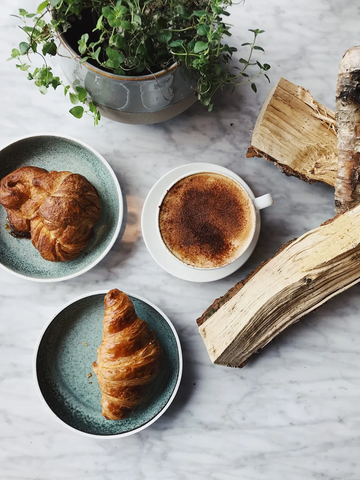 Croissants and a cinnamon-dusted cappuccino on a marble table, seen from above