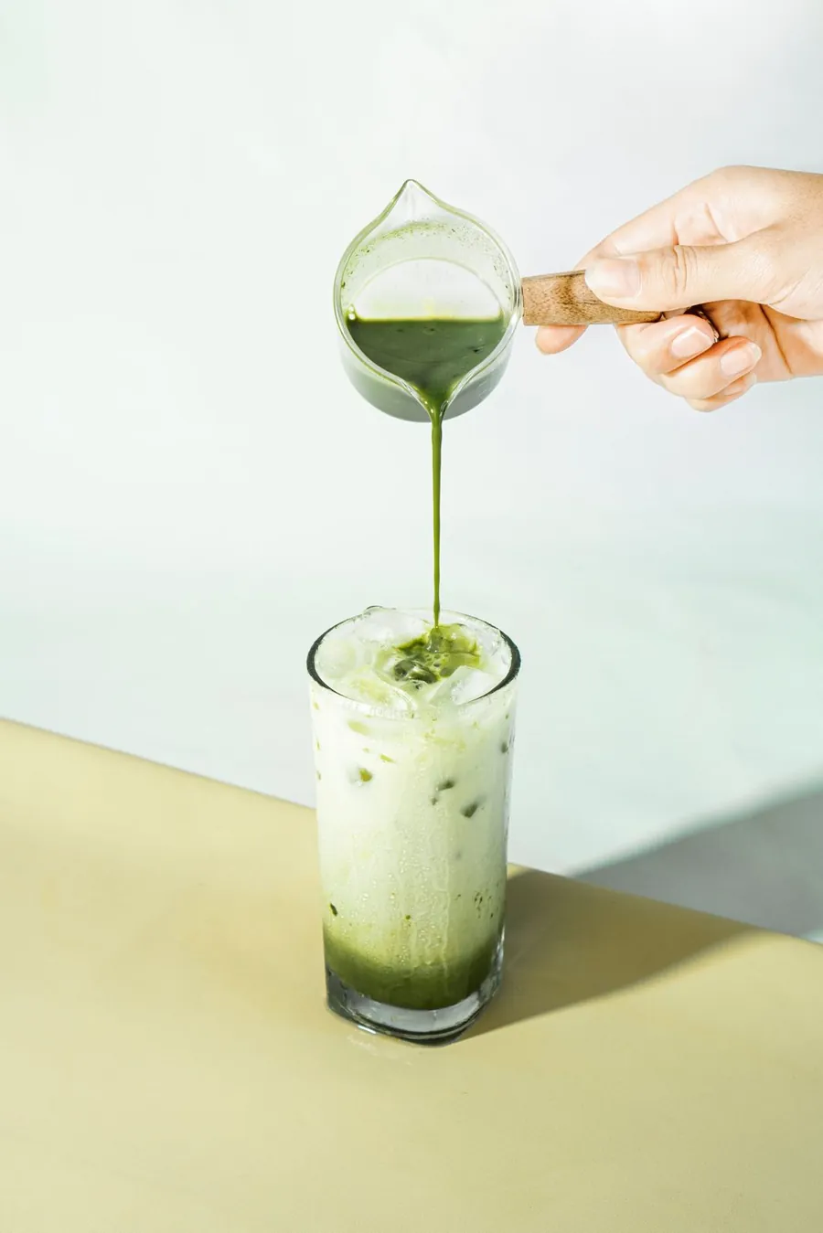 Matcha being poured over ice and milk in a tall glass
